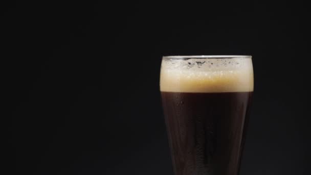 Cerveja escura fria em um copo com gotas de água — Vídeo de Stock