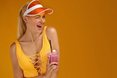 bir mayo ve şapka bir kokteyl tutan sarışın kız