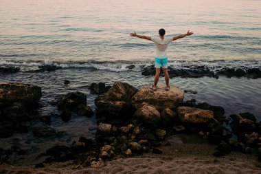 Bir dağın tepesinde elleri kaldırarak duran genç adam