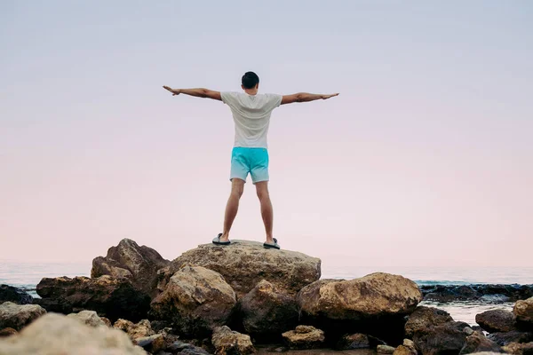 Joven de pie con las manos levantadas en la cima de un mar de montaña — Foto de Stock