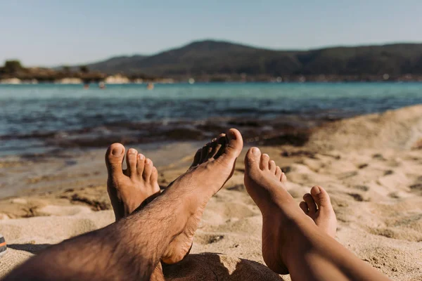 Piernas de una mujer joven y un hombre acostado en la playa en el soleado día de verano . — Foto de Stock
