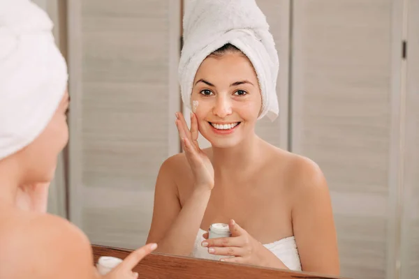 Mujer aplicando crema en su cara en el baño — Foto de Stock