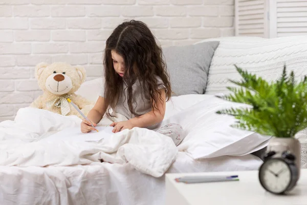 Милая маленькая девочка рисует картинки, лежа на кровати — стоковое фото