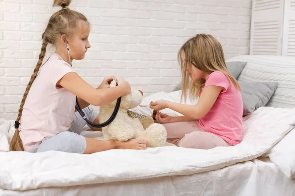 two cute children girls playing doctor with teddy bear