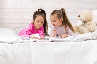 çocuklar yatakta yatarken resim çizer.