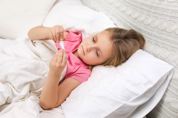 Sick little girl lying in bed with thermometer — Stock Photo, Image