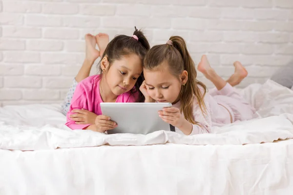 Duas crianças bonitos meninas usar tablet digital na cama . — Fotografia de Stock