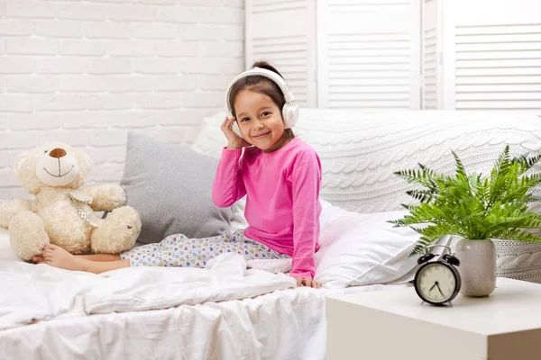 Küçük kız yatakta kulaklıklar ile müzik dinlerken. — Stok fotoğraf