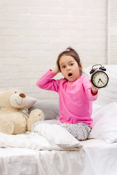 Little girl in pyjamas with clock