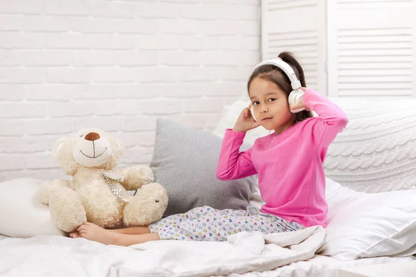 Little girl listening to the music with the headphones on bed. — Stock Photo, Image