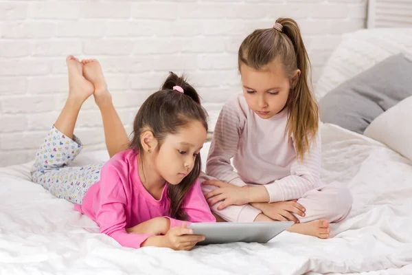 Twee schattige kinderen meisjes gebruiken digitale Tablet in bed. — Stockfoto
