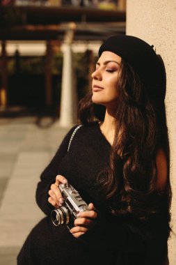Kadın elinde retro kamerayla fotoğraf çekiyor.