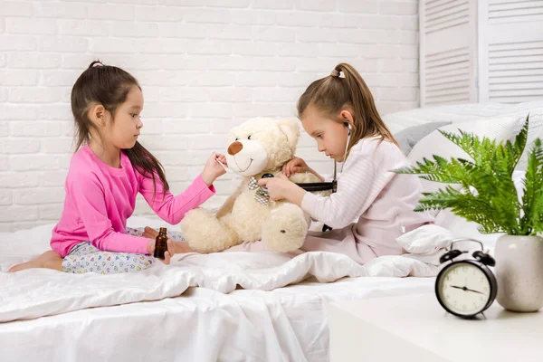 Két aranyos gyermek lányok játék orvos-val mackó otthon. — Stock Fotó