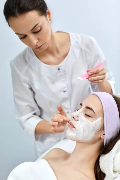 Kosmetyczka nakłada maskę na twarz kobiety — Zdjęcie stockowe
