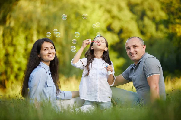 Щаслива сім'я з дитиною дме мильні бульбашки — стокове фото
