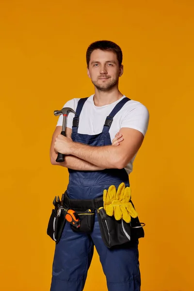 repairman worker in yellow hard hat and uniform holding hammer.