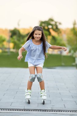 Küçük kız yaz parkında paten kayıyor..