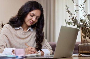 Mutlu pozitif kadın evde oturma odasında çalışırken dizüstü bilgisayar kullanıyor.