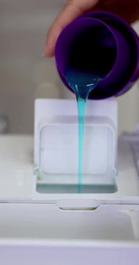 Kadın çamaşır makinesinin kompartımanına sıvı deterjan döküyor, yakın plan. yerli çamaşır makinesi