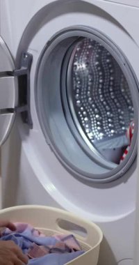Çamaşır sepetiyle evde çamaşır yıkayan kadın, çamaşır makinesinin variline renkli çamaşır yükleyen kadın..