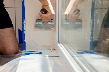 Elinde spatulası olan beyaz alçı adam pencere açılışına macun sürüyor.