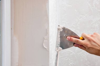 Elinde spatulası olan beyaz alçı adam pencere açılışına macun sürüyor.