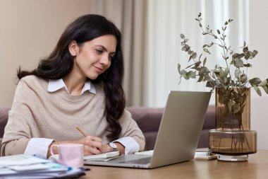 Ev ofisinde çalışan güzel bir kadın. İnternette müşterilerle iletişim kurmak için dizüstü bilgisayar kullanan bir kadın.