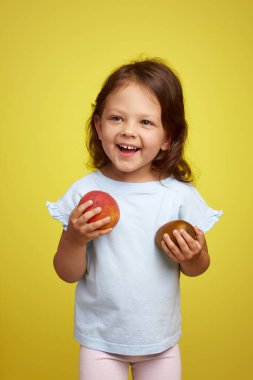 Sevimli, gülümseyen beyaz küçük kız elinde kivi ve şeftali sarısı arka planda