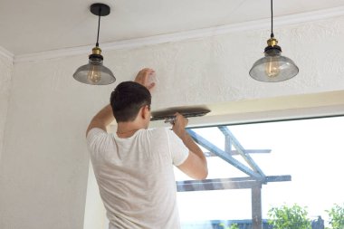 Elinde spatulası olan beyaz alçı adam pencere açılışına macun sürüyor.