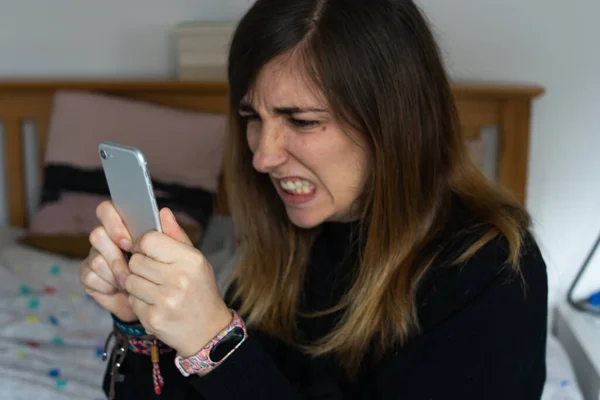 Telefonuna kızgın bir ifadeyle bakan genç ve çekici bir kadının fotoğrafı. Kötü haber.