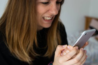 Telefonuna kızgın bir ifadeyle bakan genç ve çekici bir kadının fotoğrafı. Kötü haber.