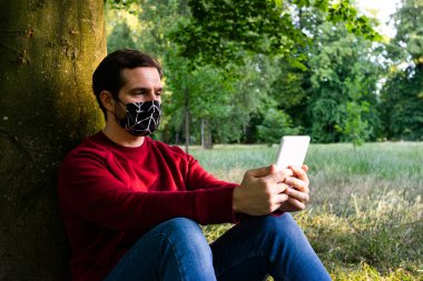Yeniden kullanılabilir yüz maskesi takan genç ve çekici bir adamın kitap okuduğu fotoğraf.