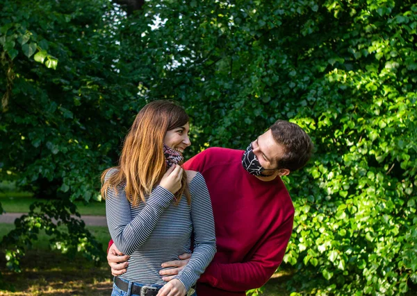 顔のマスクを着て公園でデートをしている若い魅力的なカップルの写真 笑って楽しい時間を過ごして — ストック写真