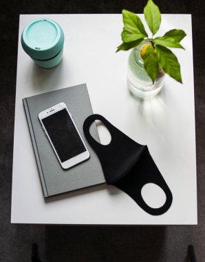 Yeniden kullanılabilir yüz maskesi, elektronik bir cihaz kahve ve beyaz bir masada bitki.