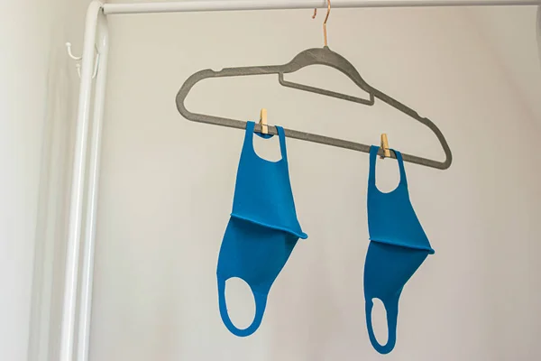 Photo of some reusable face masks colour blue and black hanging on a cloth rack while drying after washing. White background inside a house. Coronavirus outbreak