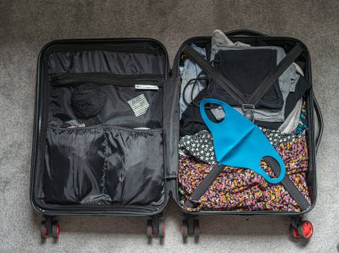 İçinde yaz kıyafetleri, pasaport ve yeniden kullanılabilir yüz maskesi olan bir valizin fotoğrafı.. 