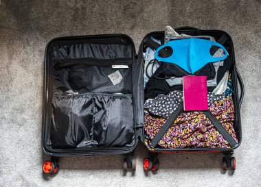 İçinde yaz kıyafetleri, pasaport ve yeniden kullanılabilir yüz maskesi olan bir valizin fotoğrafı.. 