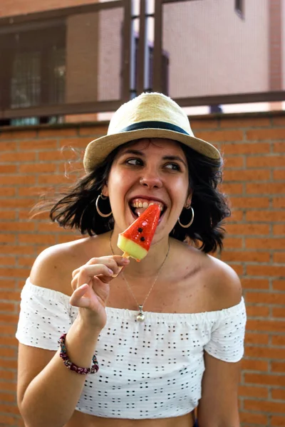 照片中 一个年轻而迷人的女人 留着短发 头戴帽子 吃着西瓜形状的冰淇淋 穿着夏装 — 图库照片