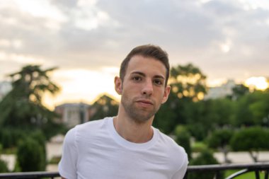 Genç ve çekici bir adamın fotoğrafı. Parkta duruyor. Çok modern giysileri var.