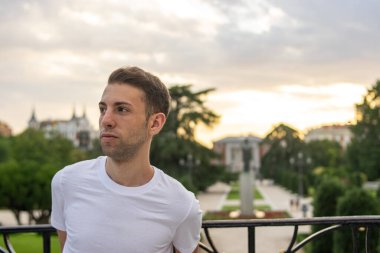 Genç ve çekici bir adamın fotoğrafı. Parkta duruyor. Çok modern giysileri var.