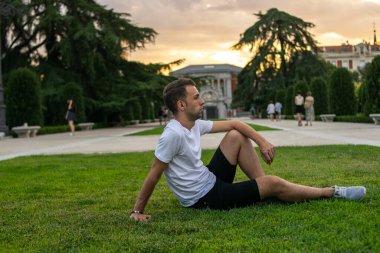 Genç ve çekici bir adamın fotoğrafı. Çimlerin üzerinde rahatça oturup ufka bakıyor.