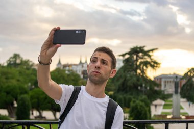 Sırt çantası takan ve güzel bir çevrede selfie çeken genç ve çekici bir adamın fotoğrafı.. 