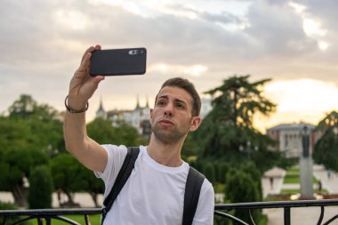 Sırt çantası takan ve güzel bir çevrede selfie çeken genç ve çekici bir adamın fotoğrafı.. 
