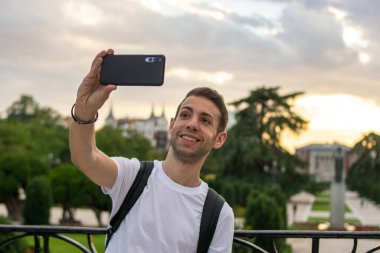 Sırt çantası takan ve güzel bir çevrede selfie çeken genç ve çekici bir adamın fotoğrafı.. 