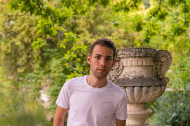 Doğanın ortasında taş bir heykelin yanında pansiyoner suratı olan genç ve çekici bir adamın fotoğrafı.