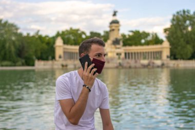 Telefonda konuşan ve beyaz tişört giyen genç ve çekici bir adamın fotoğrafı.