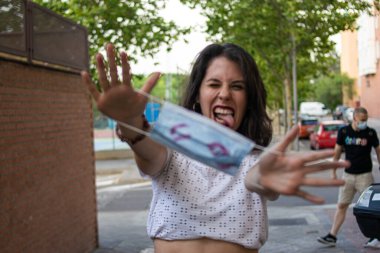 Genç ve çekici bir kadının fotoğrafı. Tek kullanımlık mavi maskesiyle dudakları rujla kaplı ve mutlu görünüyor.