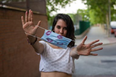 Genç ve çekici bir kadının fotoğrafı. Tek kullanımlık mavi maskesiyle dudakları rujla kaplı ve mutlu görünüyor.
