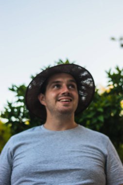 Sakallı, kahverengi şapkalı ve yüzünde gülen bir yüzle bankta oturan genç ve çekici bir adamın portresi. Bahçe, park, tatil fotoğrafları..