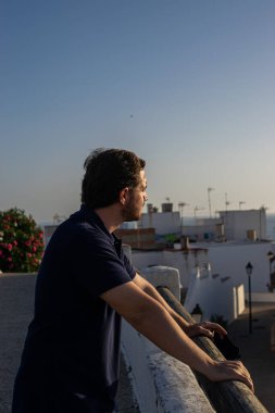 Yüz maskesi takan genç ve çekici bir adamın fotoğrafı. Conil 'in manzarasından keyif alıyor. Beyaz evler, Coronavirus salgını sırasında turizm yapıyorlar. Sosyal mesafe ve izolasyon